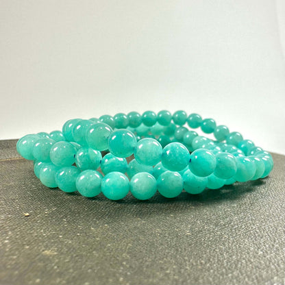 Turkis perlekæde lagt på en grå overflade med en enkel hvid baggrund.