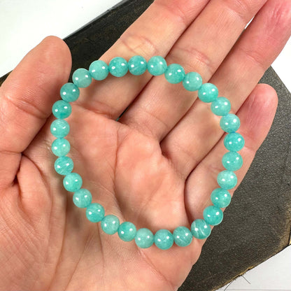 En hånd holder et armbånd af turkisfarvede perler mod en mørk baggrund.