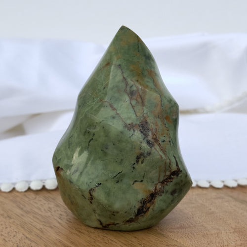 Chrysopras flamme på træbord med hvid baggrund. Grøn farve med naturlige mønstre og ujævn form.