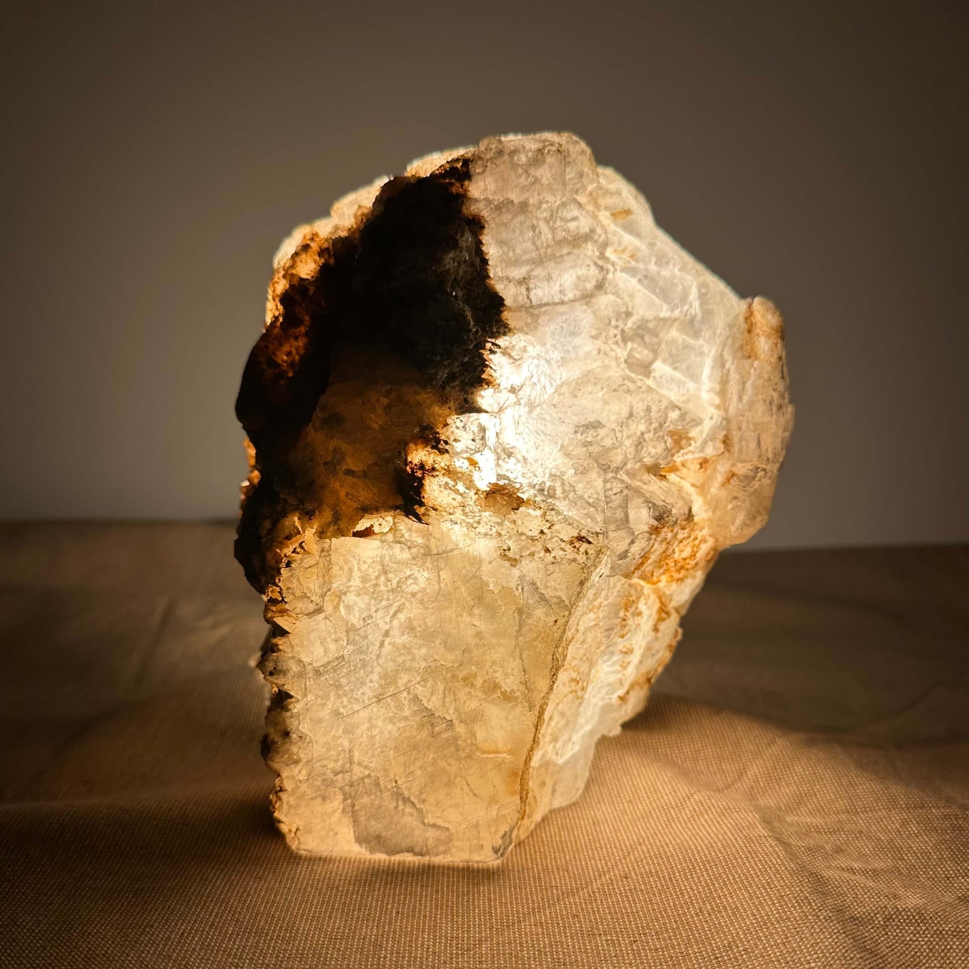 Klump af halvgennemsigtigt mineral med mørke pletter, oplyst dramatisk mod en enkel baggrund.