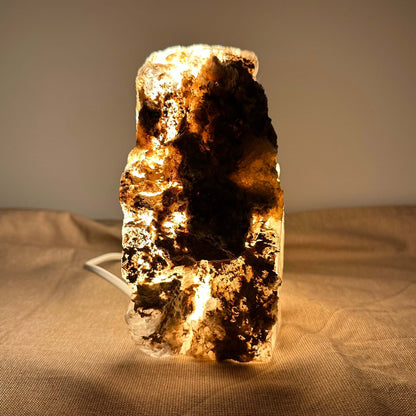 En oplyst, krystallignende stenlampe på et blødt, beige stof baggrund.