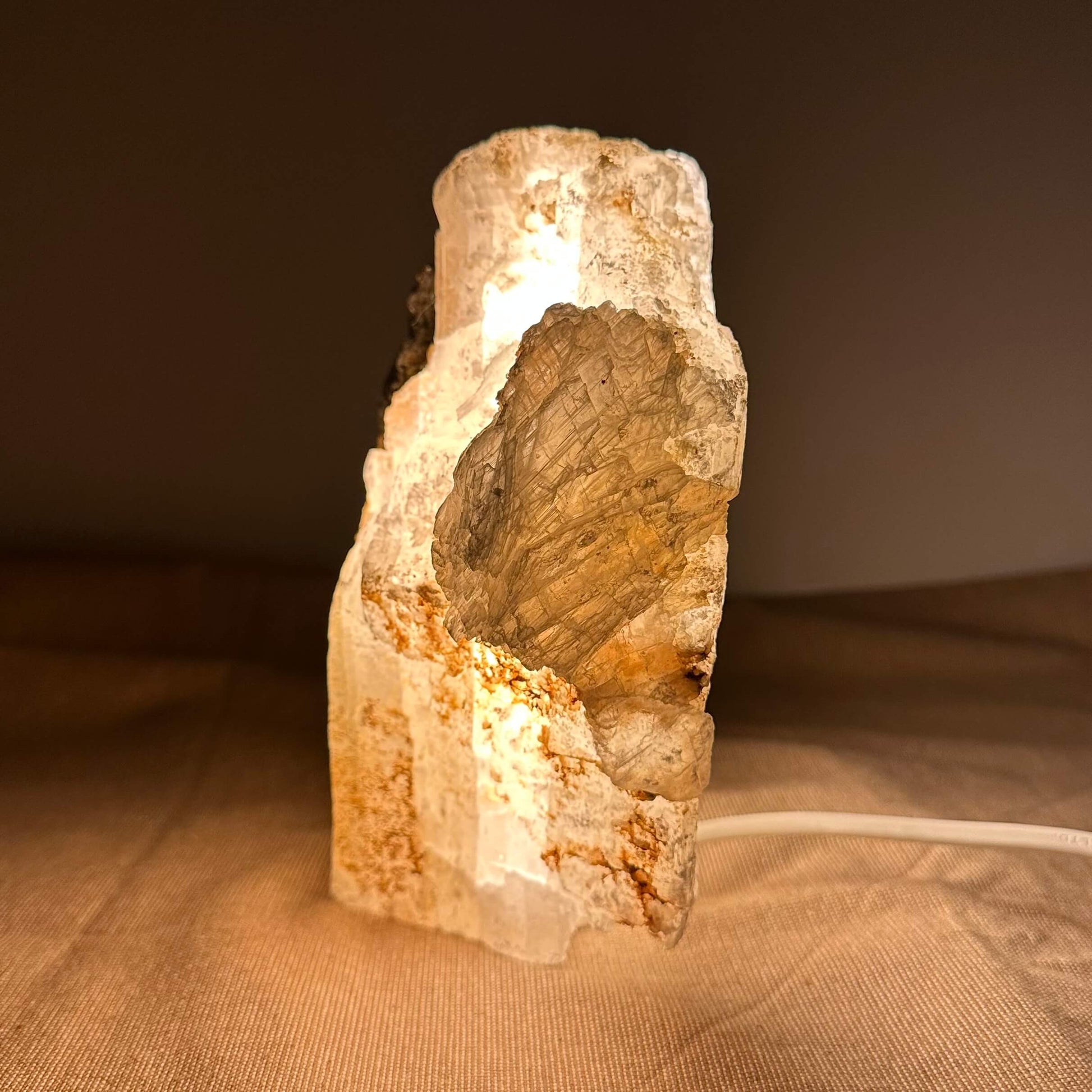 En oplyst krystalstenskulptur på beige baggrund med synlig ledning.