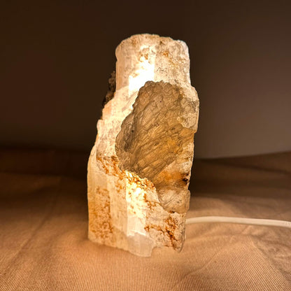 En oplyst krystalstenskulptur på beige baggrund med synlig ledning.