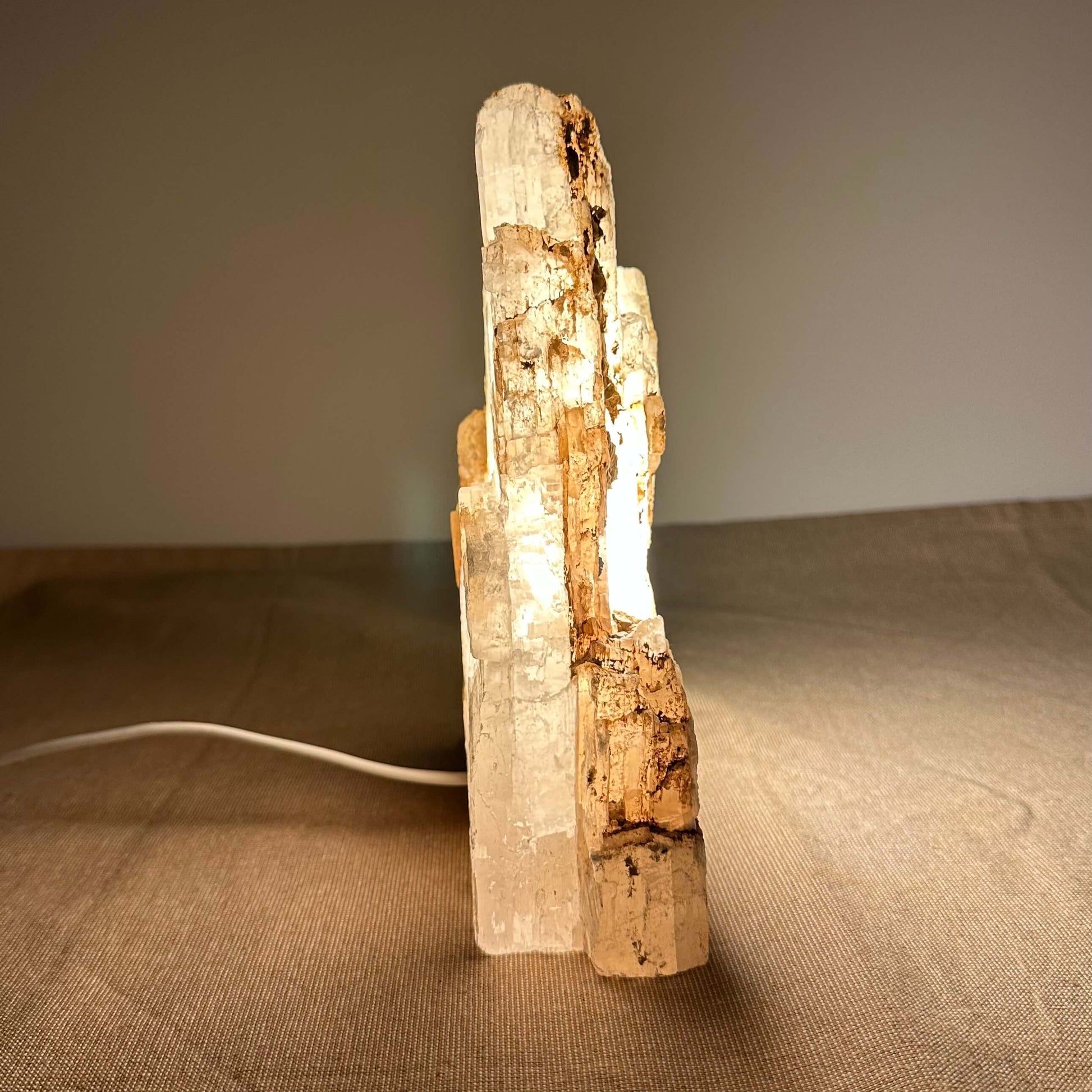 En lampe lavet af en lysende selenitkrystal på et bord med en neutral baggrund.