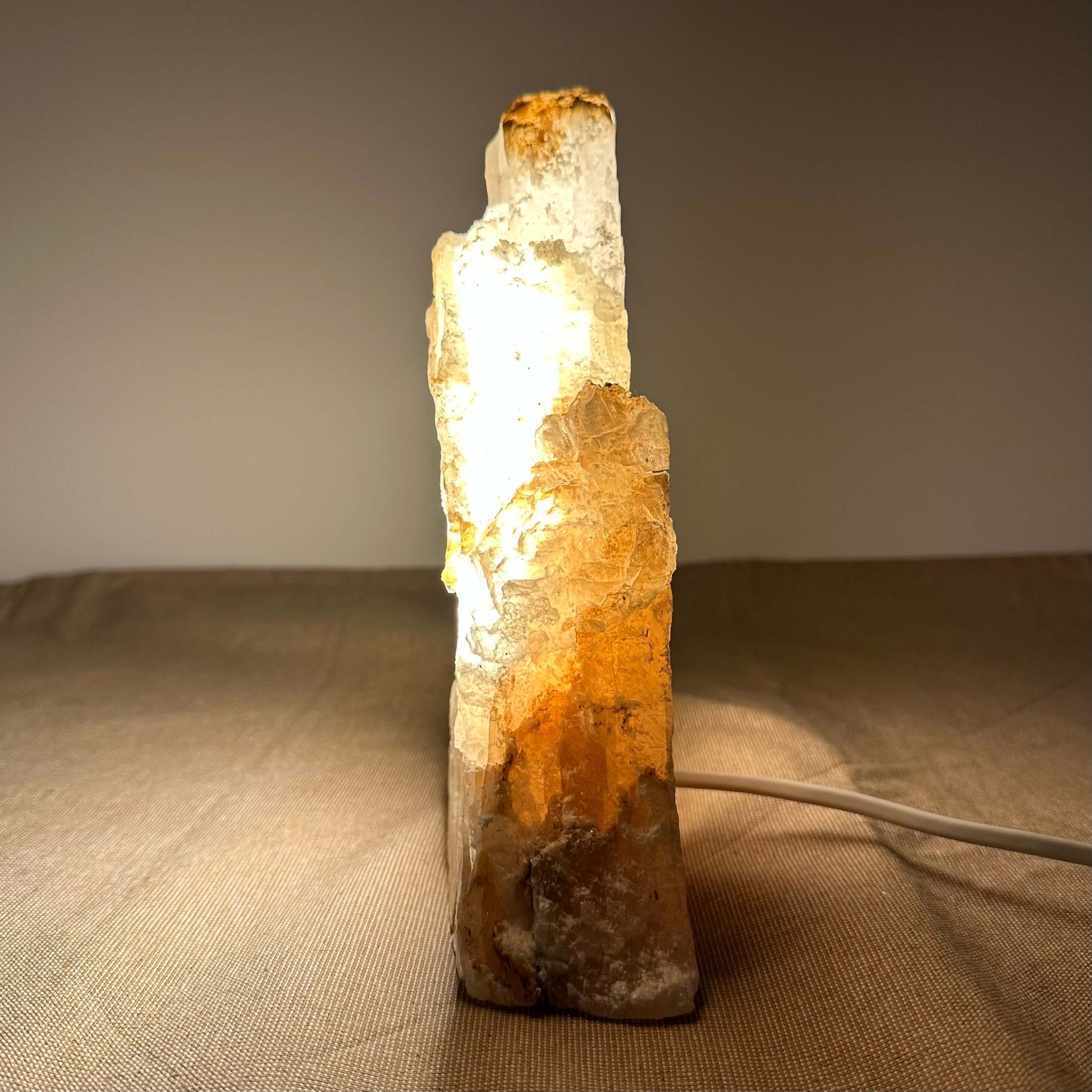 En oplyst krystallampe med orange nuancer står på et bord med en lys ledning bagved.