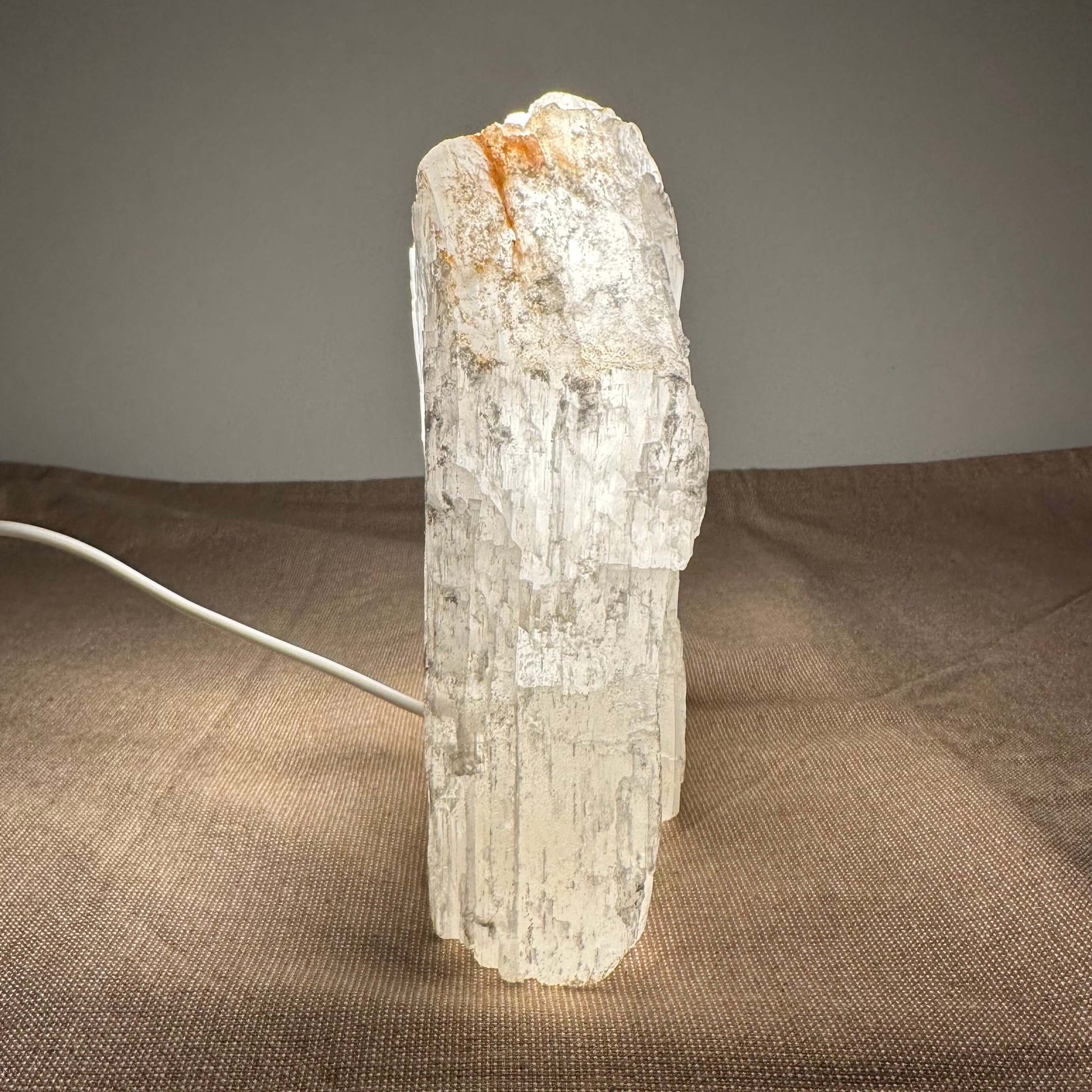 En oplyst selenit-lampe på et bord med brun dug.