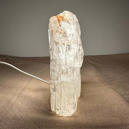 En oplyst selenit-lampe på et bord med brun dug.