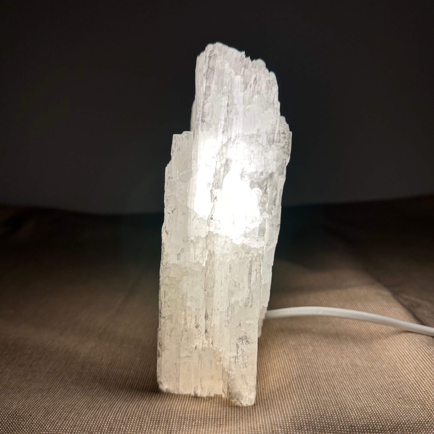 En oplyst selenitkrystal på et bord, med en mørk baggrund og klart lys indeni.
