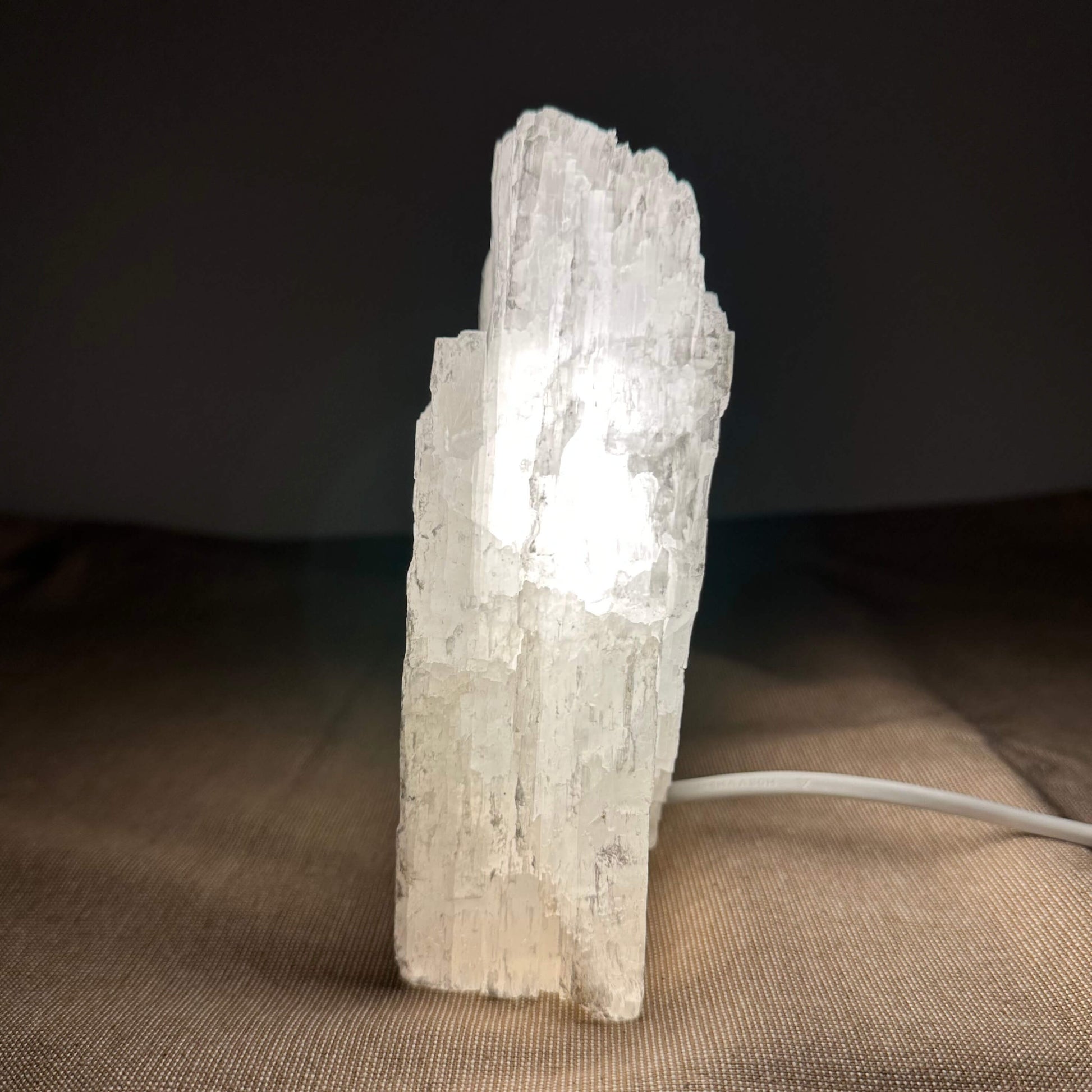 En oplyst selenitkrystal på et bord, med en mørk baggrund og klart lys indeni.