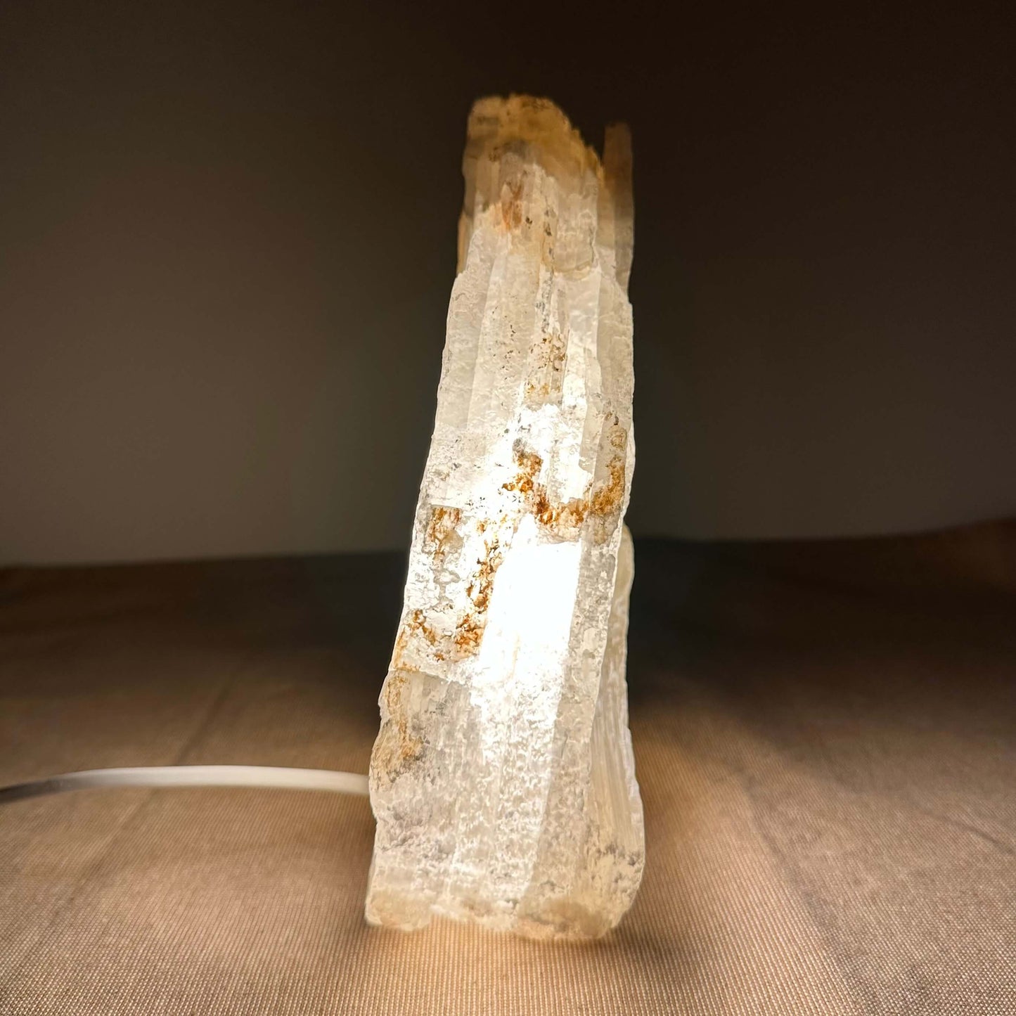 Klart, oplyst krystal på en brun overflade mod mørk baggrund.