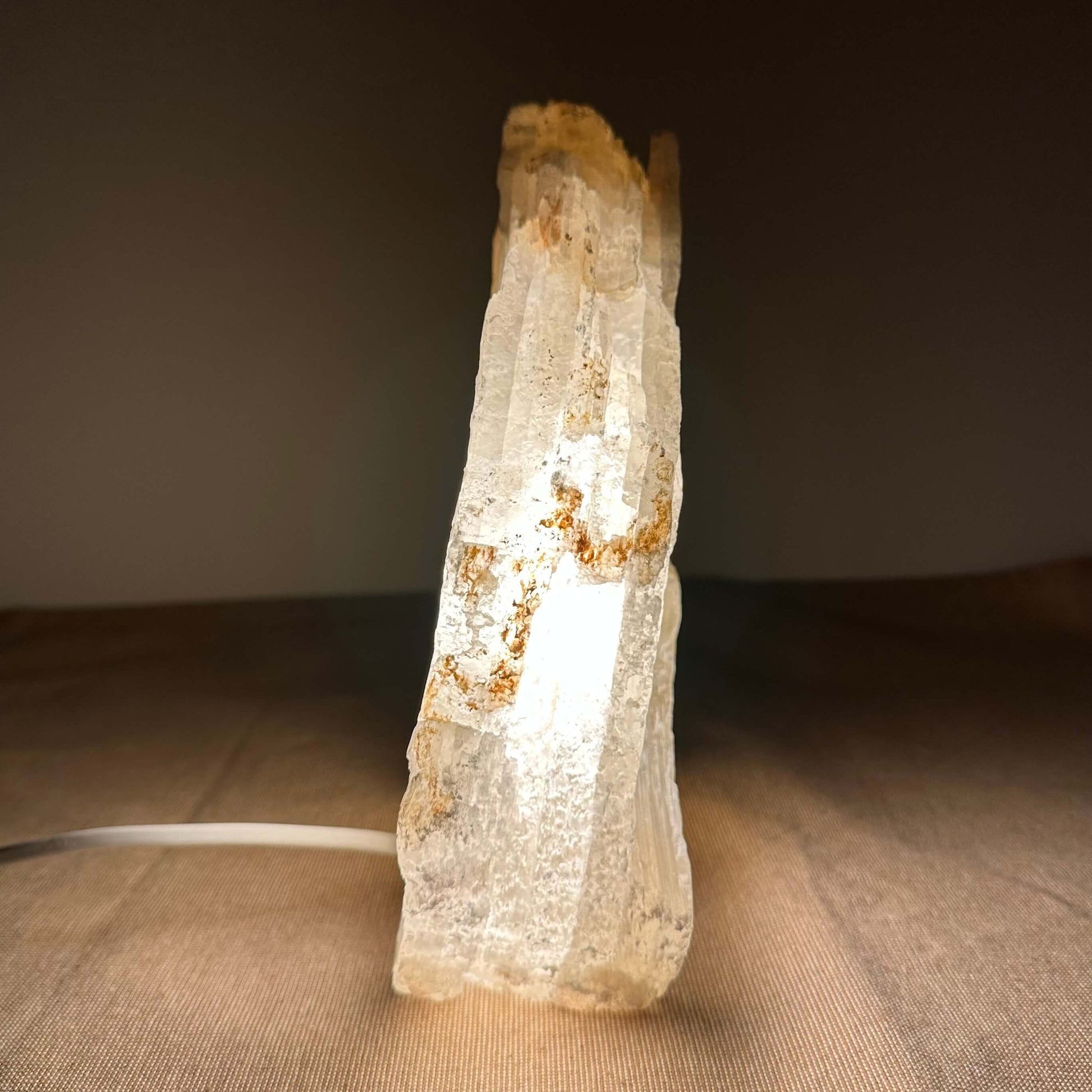 Klart, oplyst krystal på en brun overflade mod mørk baggrund.