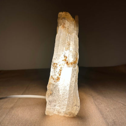 Klart, oplyst krystal på en brun overflade mod mørk baggrund.