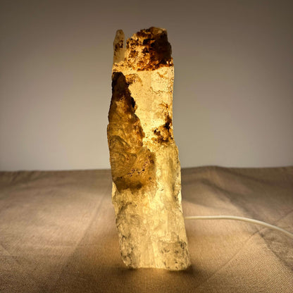 En oplyst selenitkrystallampe står på et bord, der kaster et varmt og hyggeligt lys i rummet.