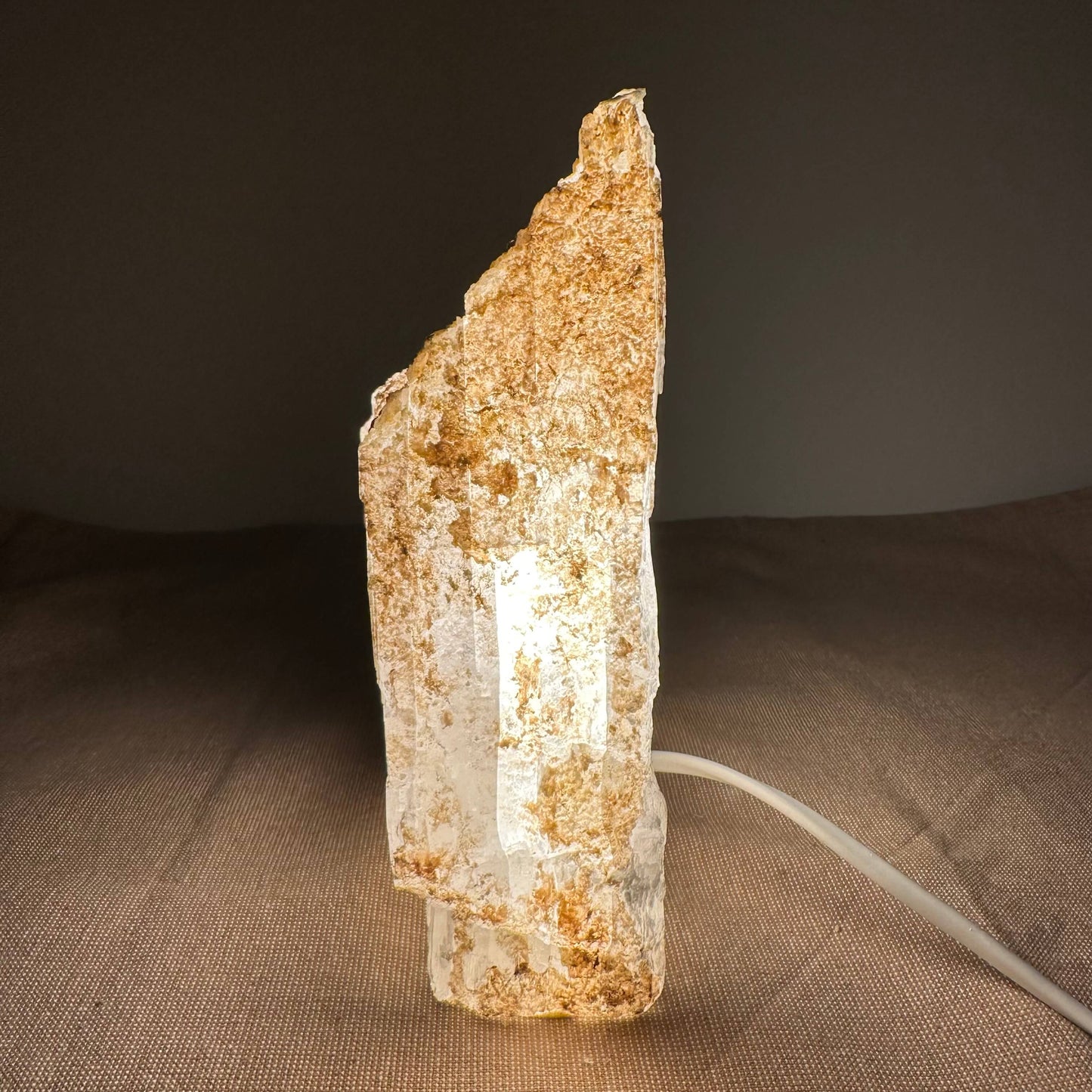 Et lysende selenitkrystal placeret på en mørk baggrund, med en ledning synlig på højre side.