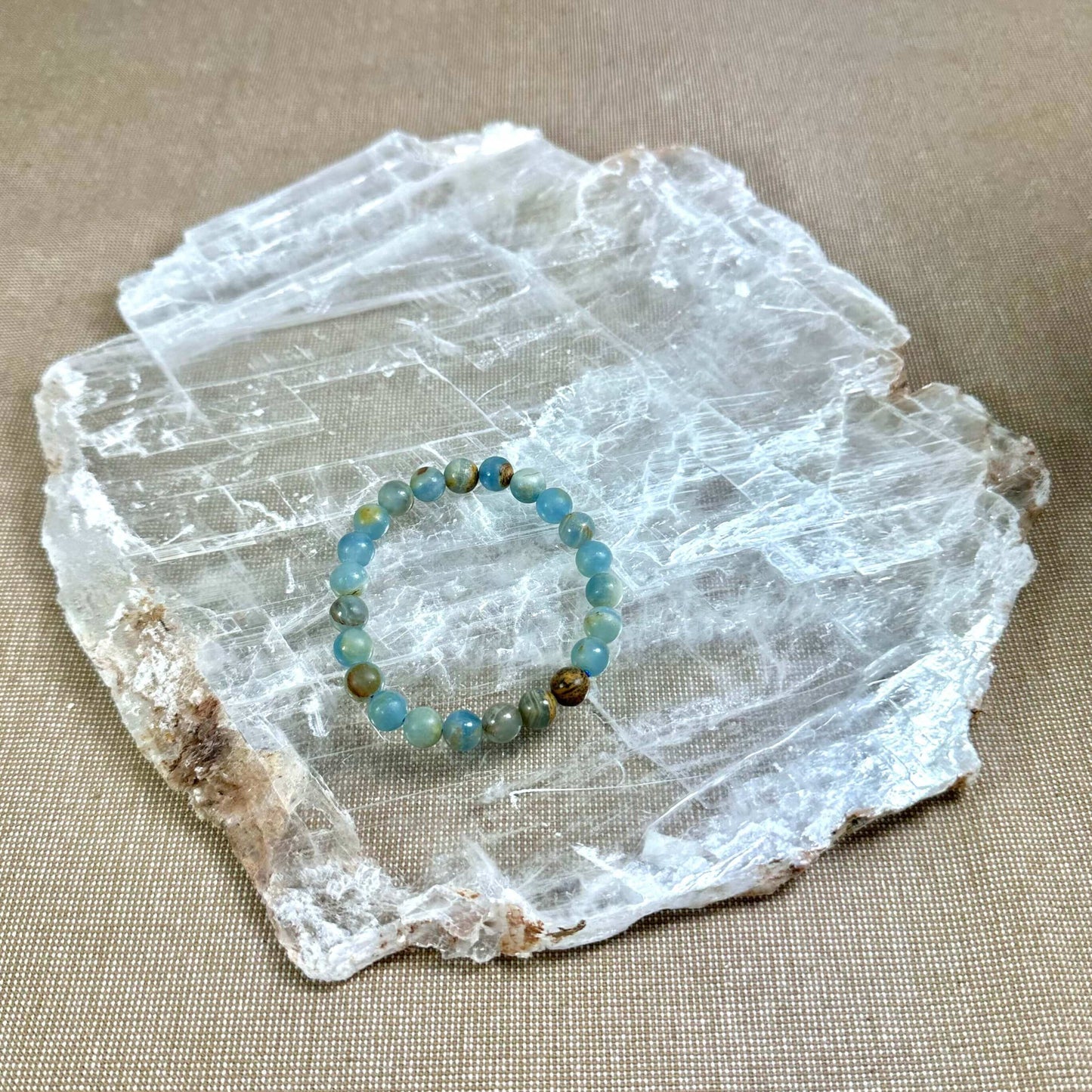 Blåt armbånd af perler placeret på et stort, fladt stykke krystal på en beige overflade.