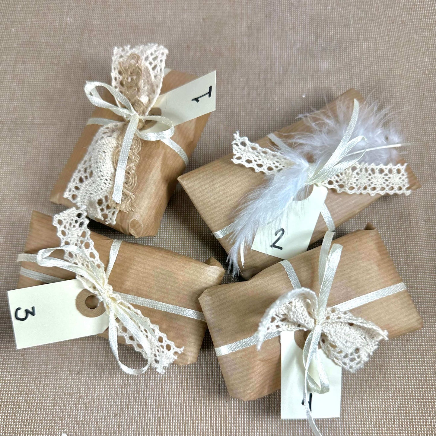 Brune gaver med blonder og numre 1 til 4, dekoreret med bånd og en fjer på beige baggrund.