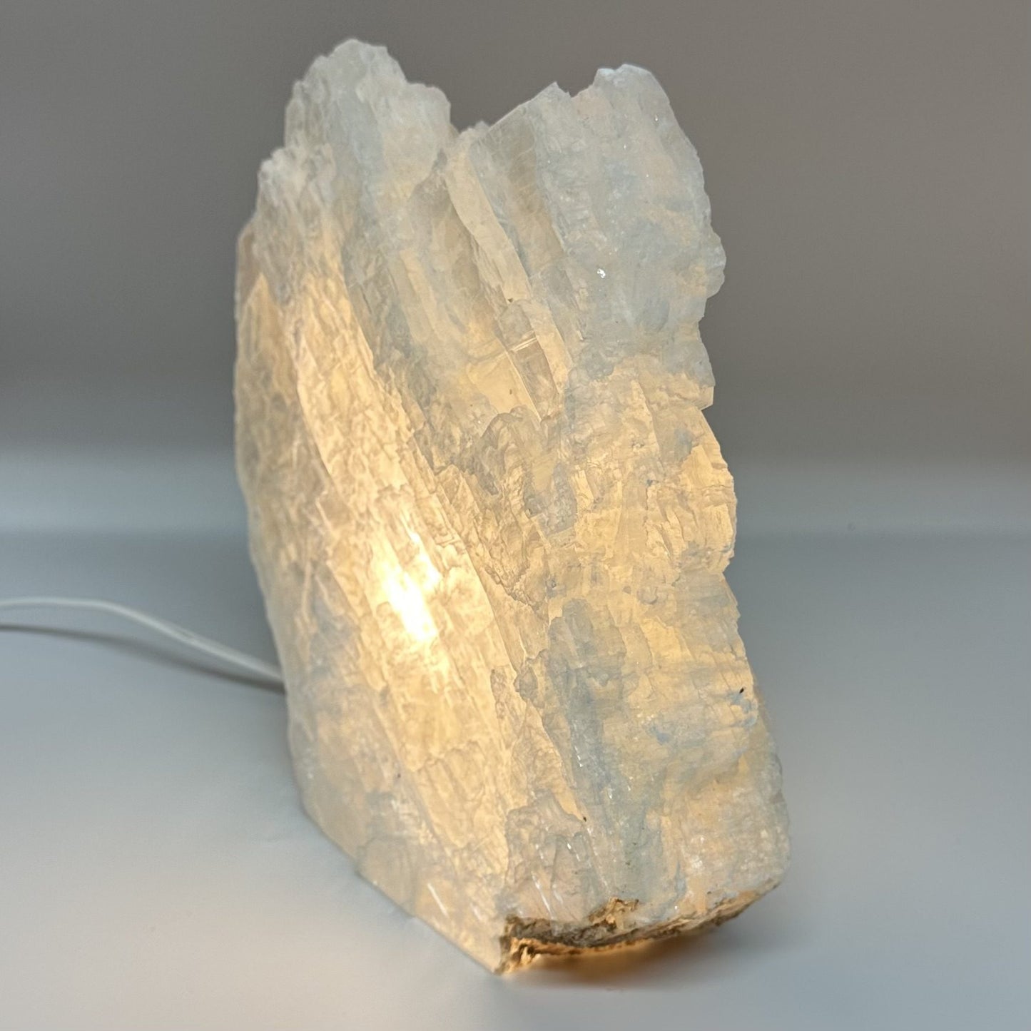Mexicansk Selenit lampe nr 20 lyser op i varm glød, formet som en naturlig sten med kabel synlig.