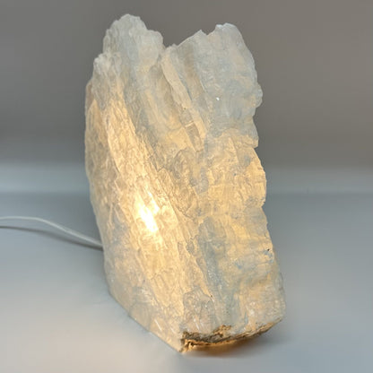 Mexicansk Selenit lampe nr 20 lyser op i varm glød, formet som en naturlig sten med kabel synlig.