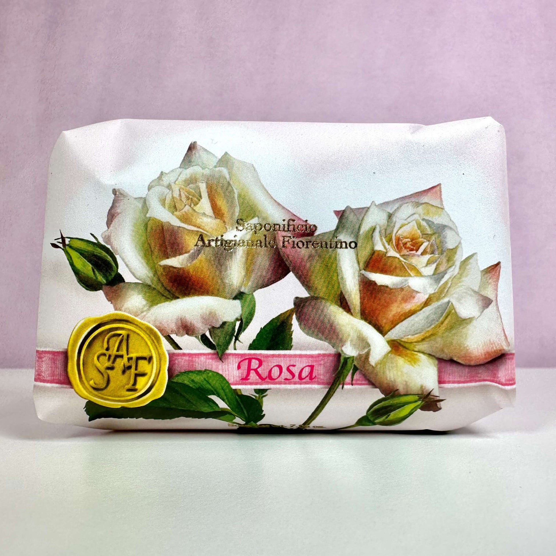 Fiorentino Rosa håndsæbe er elegant indpakket i papir med et smukt design af lyserøde og hvide roser. På forsiden ses teksten "Sapone Artigianale Fiorentino" samt et gult segl med initialerne "SAF". Den romantiske emballage udstråler italiensk luksus og klassisk charme, hvilket understreger sæbens eksklusive kvalitet. En duftende hyldest til naturlig skønhed og forkælelse af hænderne.
