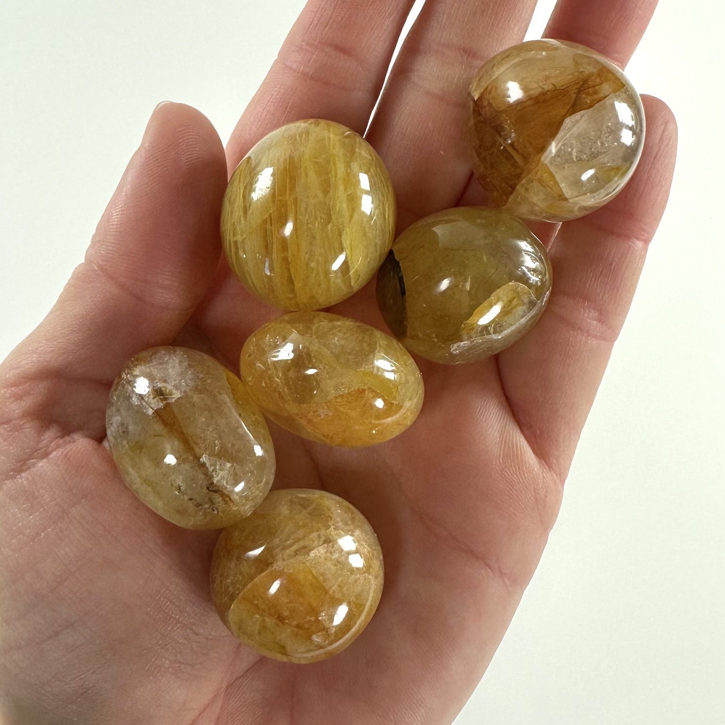 Hånd holder seks glatte Golden Healer lommesten i forskellige nuancer af gyldent gult.