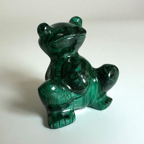 En skulptur af en frø udskåret i malakit viser de karakteristiske grønne og sorte mønstre på en lys baggrund.
