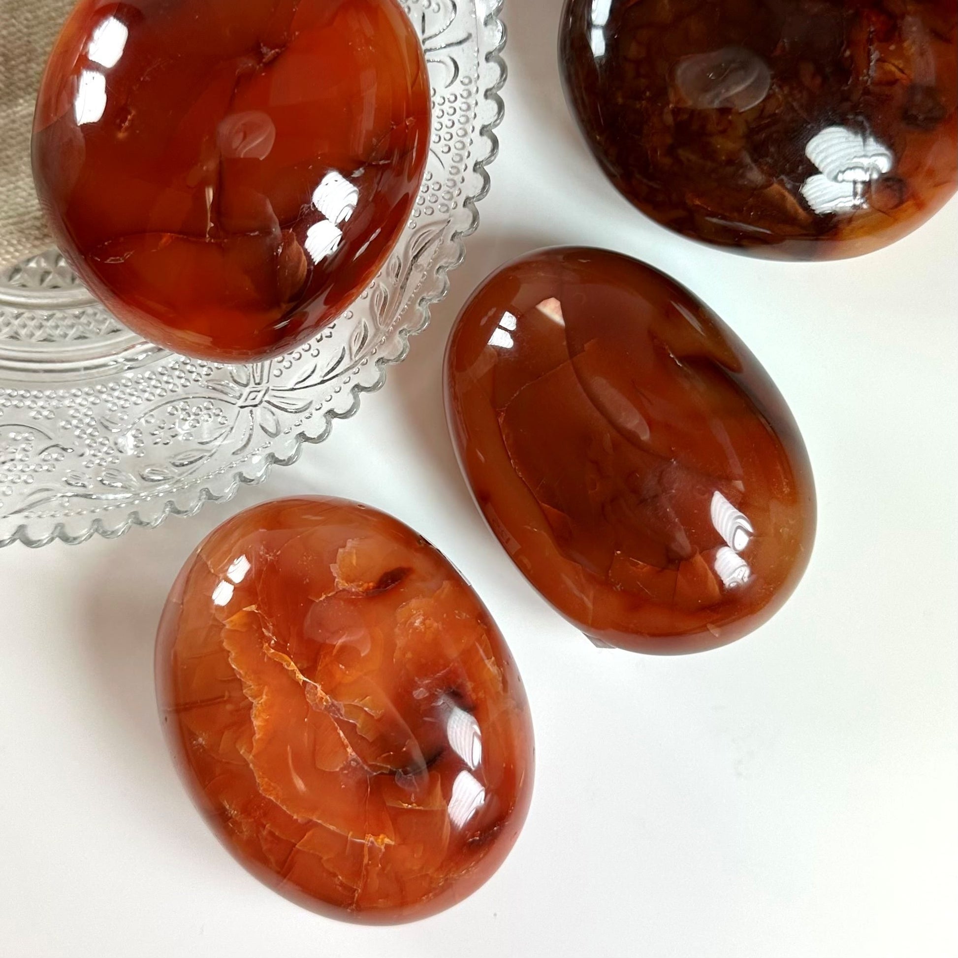 Karneol palmesten på glasfad og bord, skinner i røde og orange nuancer.