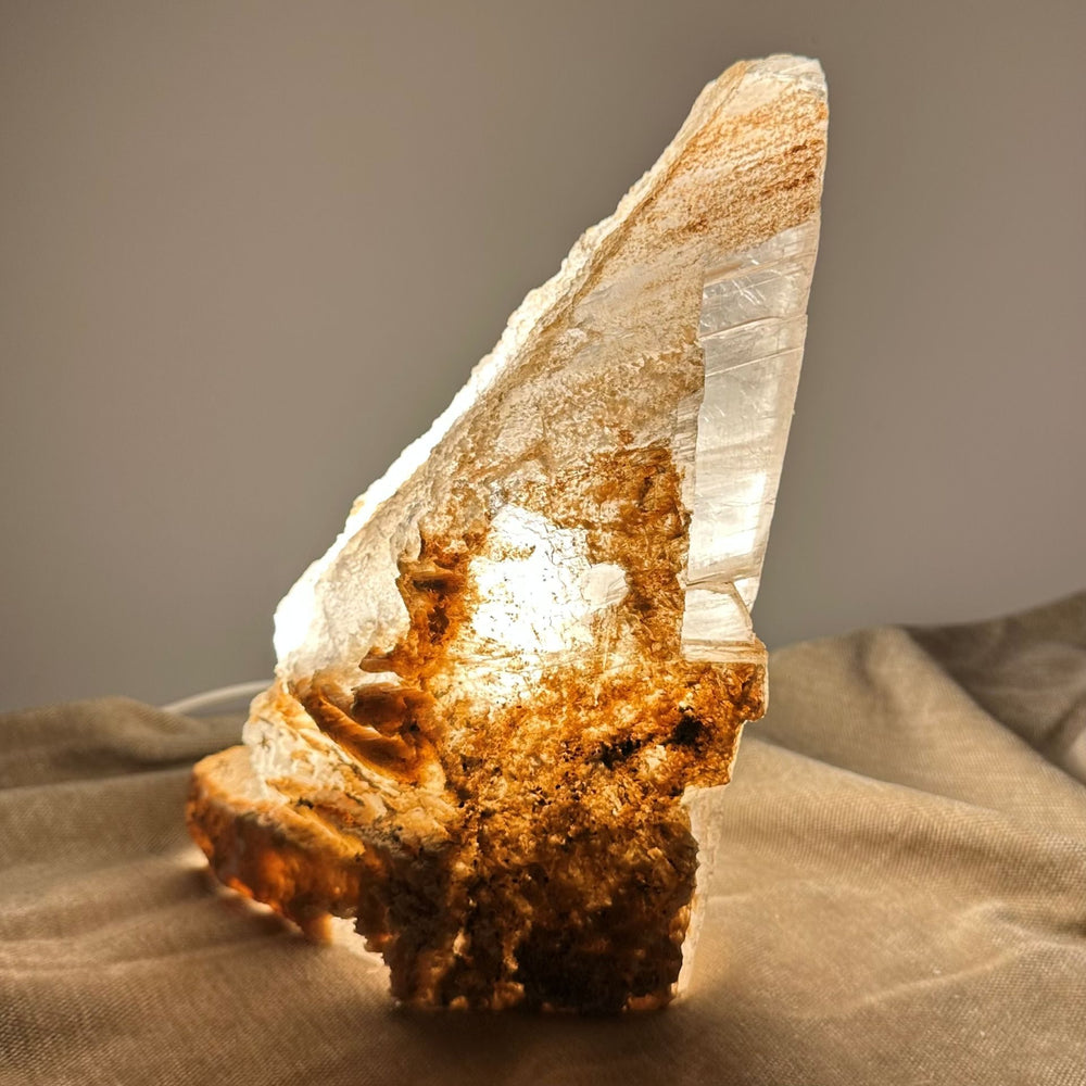 Mexicansk Selenit lampe nr 49 i naturlig, ujævn form på stofoverflade, oplyst indefra og udstråler varmt lys.