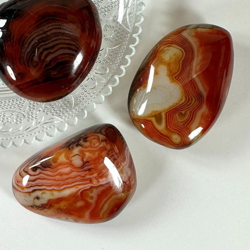 Tre Sardonyx palmsten på en glastallerken, med rige orange og røde toner og naturlige mønstre.
