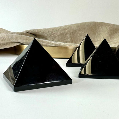 Sort obsidian pyramide på lys baggrund med blødt stof og gylden bog i baggrunden.