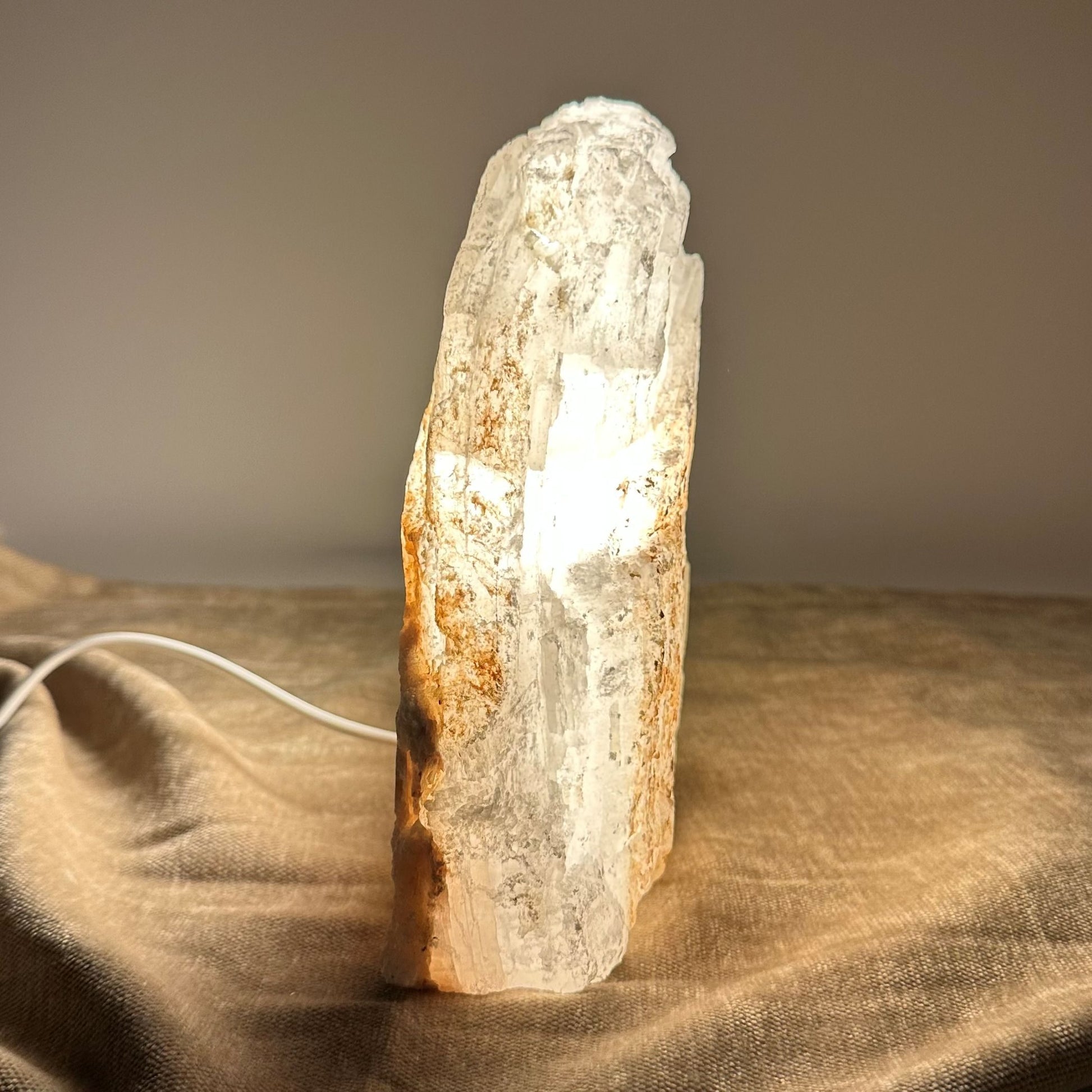Mexicansk Selenit lampe nr 1: En oplyst selenit lampe i en naturlig form står på en beige overflade med en ledning ved siden af.