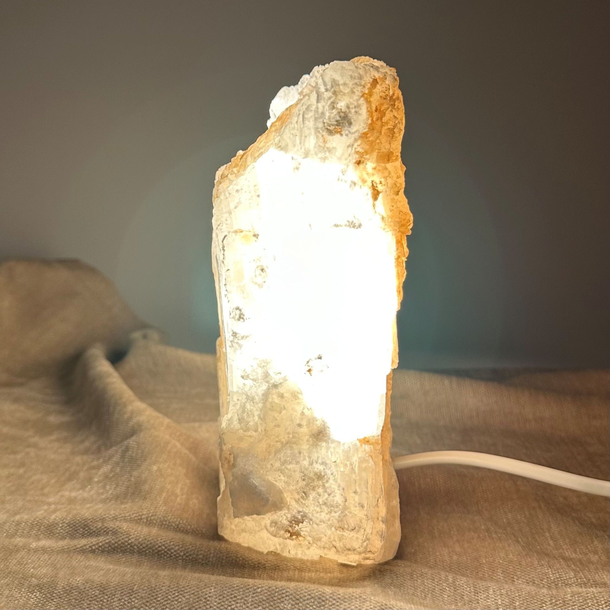 Mexicansk Selenit lampe nr 25 lyser varmt op på en tekstureret overflade, med ledning synlig for tilslutning.