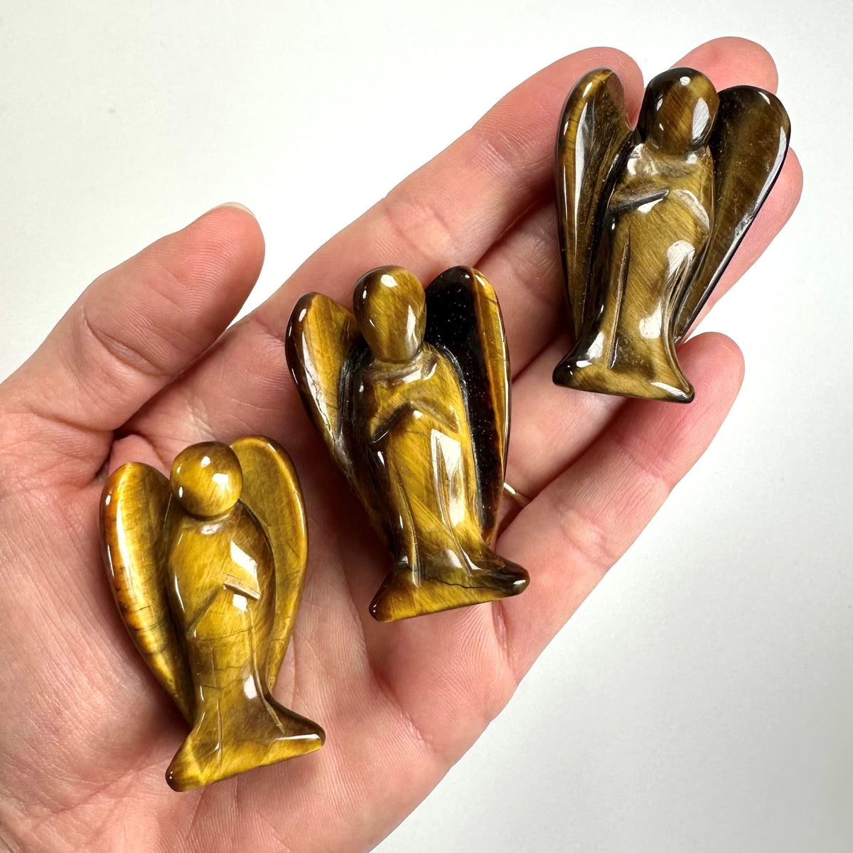 Hånd med tre Tigerøje engle, poleret stenfigur med gyldne og brune nuancer.