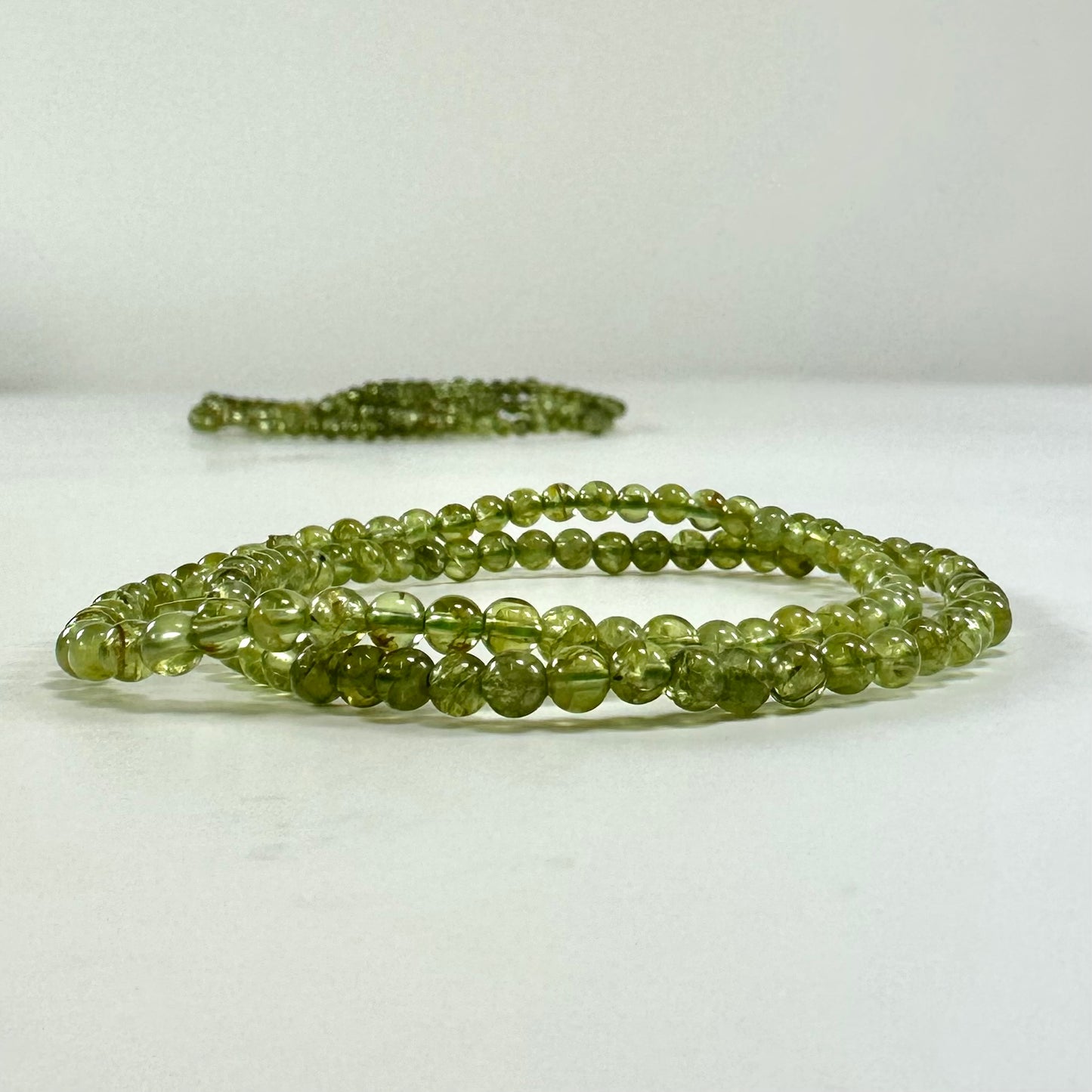 Peridot armbånd i grønne nuancer, lagt på en lys overflade. Armbåndet består af runde perler.