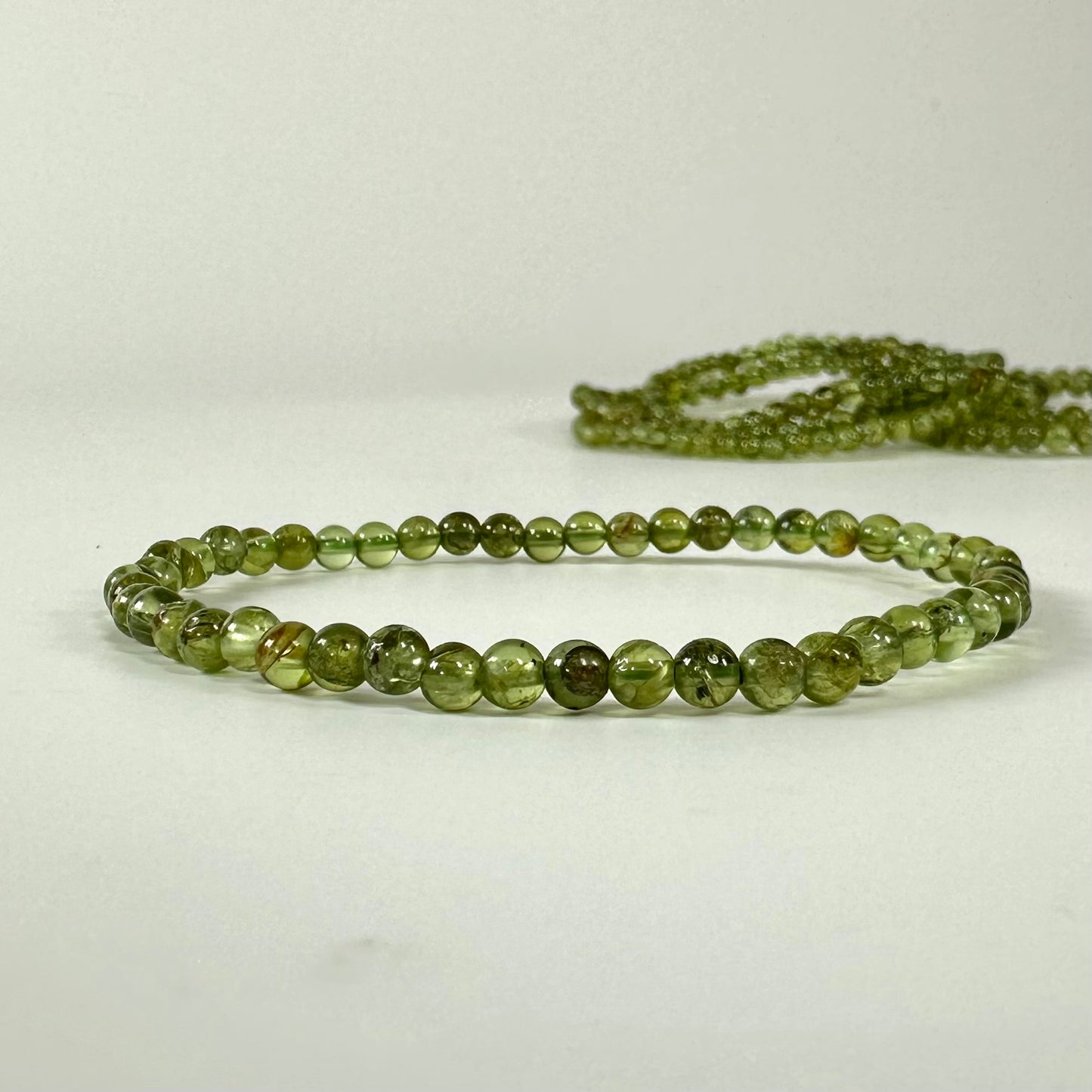 Peridot armbånd lavet af grønne perler ligger på en lys overflade.