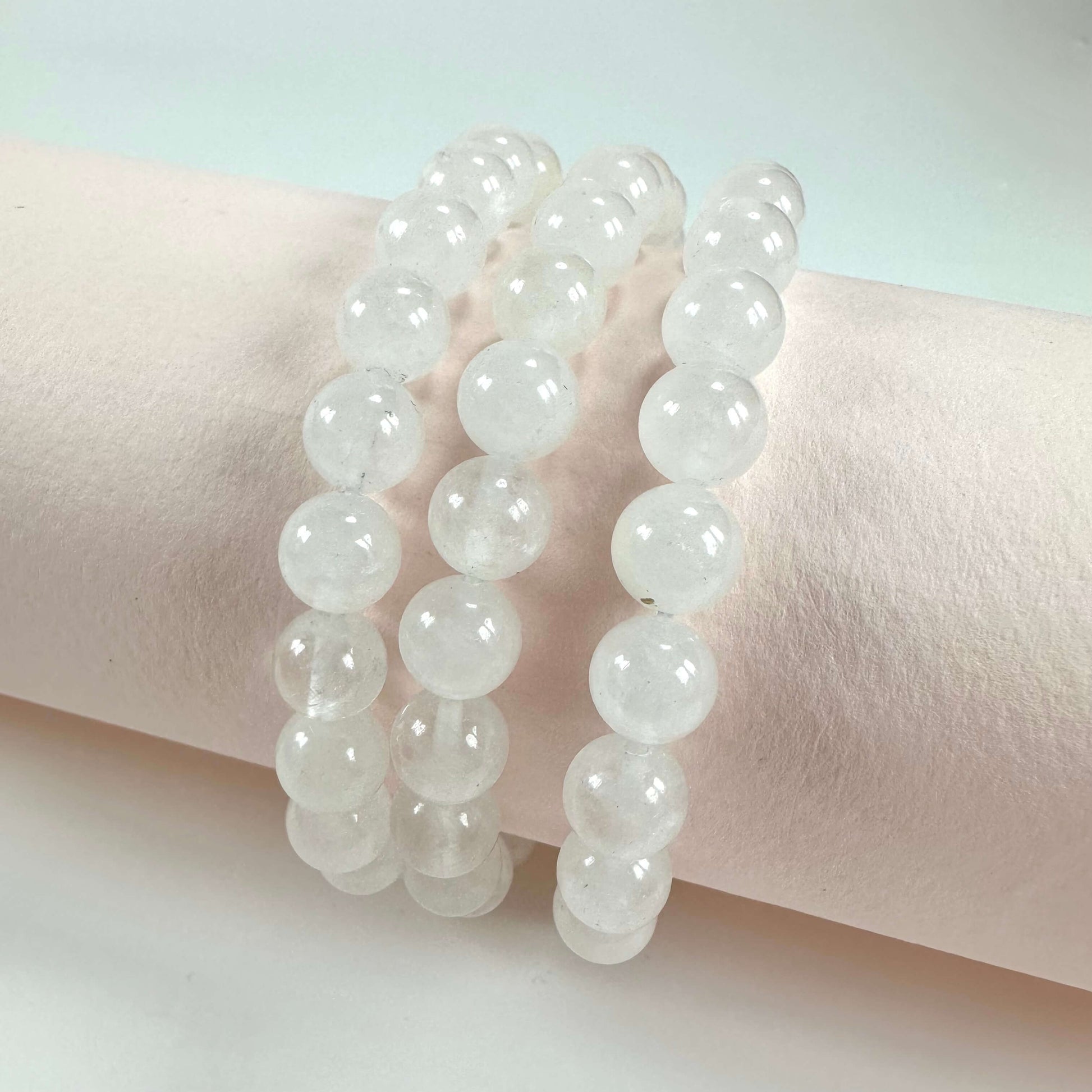 Tre rækker af bjergkrystal armbånd præsenteret på en cremefarvet baggrund.