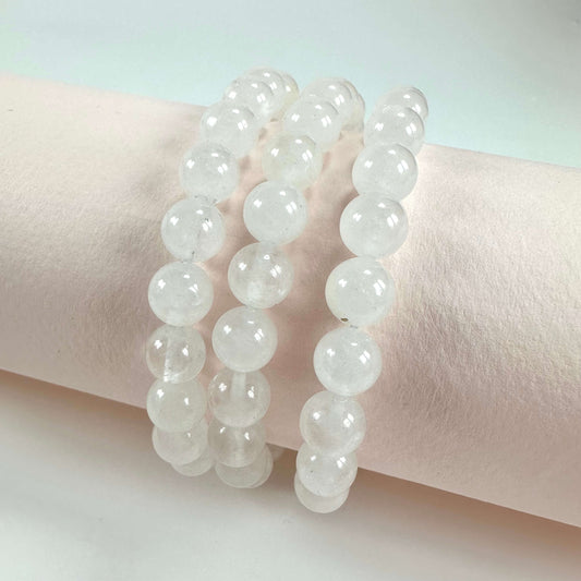 Tre rækker af bjergkrystal armbånd præsenteret på en cremefarvet baggrund.