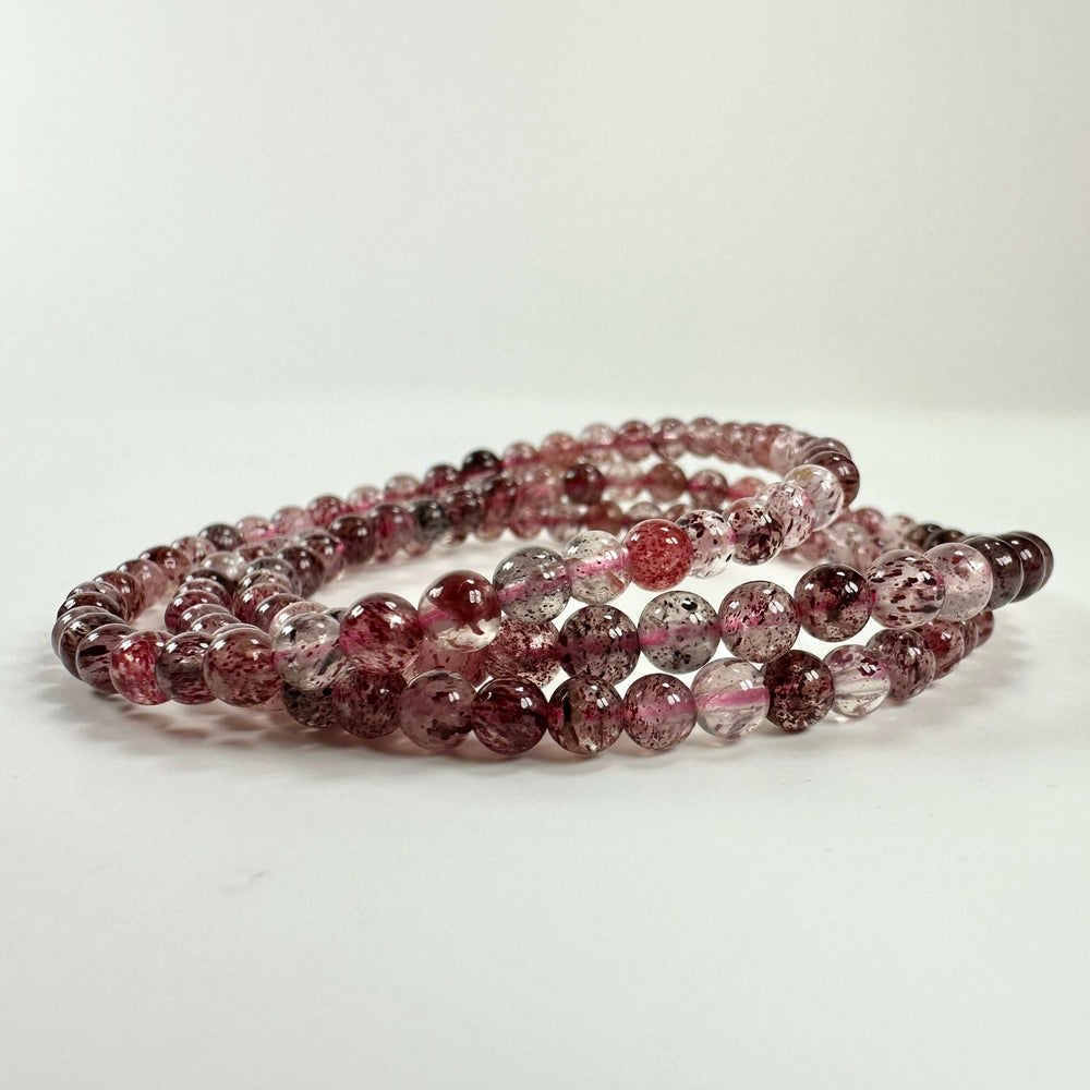 Jordbærkvarts armbånd med delikate lyserøde og røde perler på hvid baggrund.