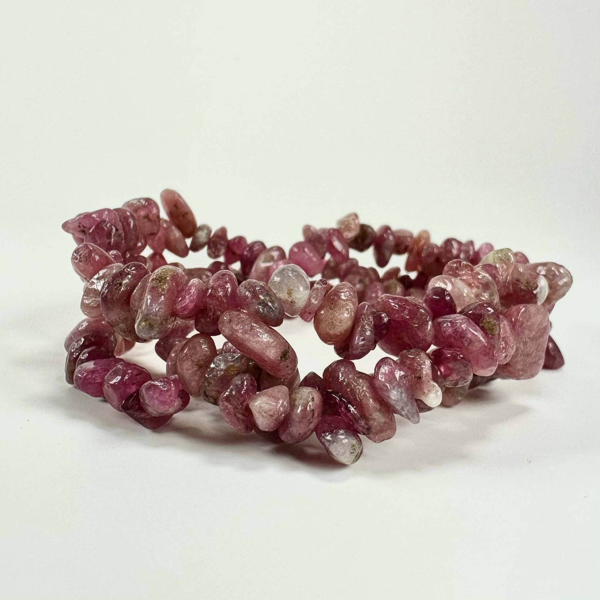 Pink turmalin armbånd med polerede sten i nuancer af rosa og rød, lagt på en hvid baggrund.