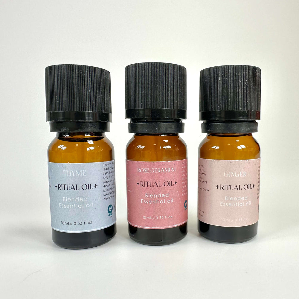 Flasker med æteriske olier: timian, rose geranium og ingefær, hver med sort låg og etiketter i forskellige farver.
