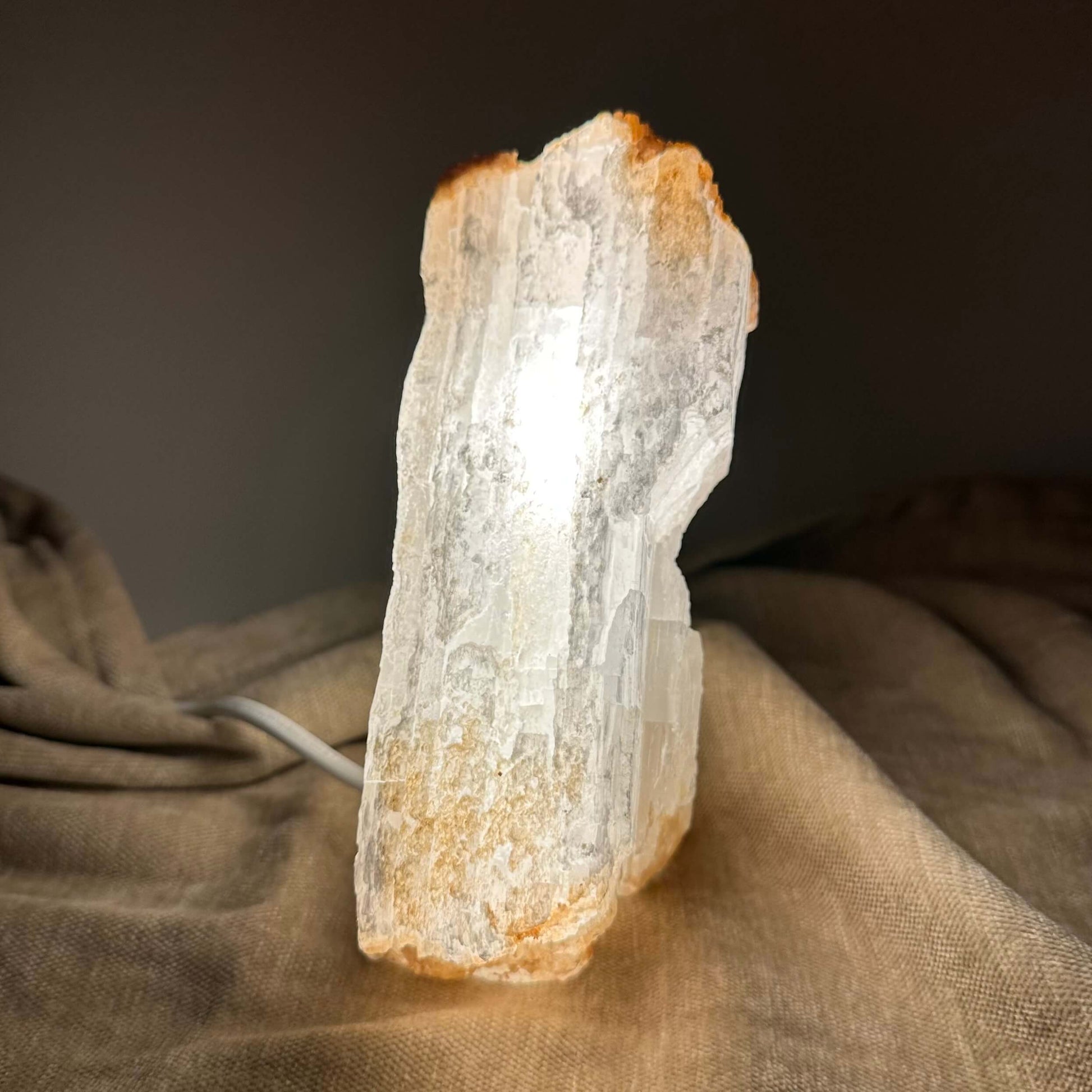 Selenitlampe lyser op mod en mørk baggrund, placeret på en brun klud.