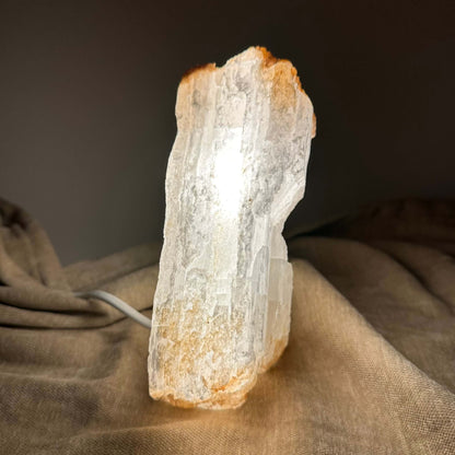 Selenitlampe lyser op mod en mørk baggrund, placeret på en brun klud.