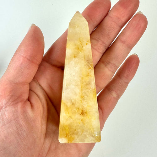 Hånd holder en Golden Healer-obelisk med gule og hvide nuancer på en neutral baggrund.