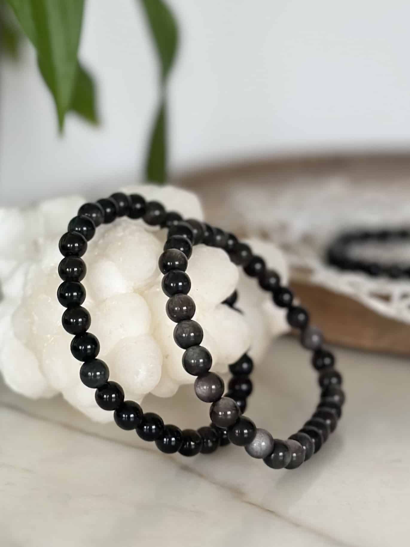 To obsidian sølv armbånd ligger på en hvid sten, omgivet af grønne blade.