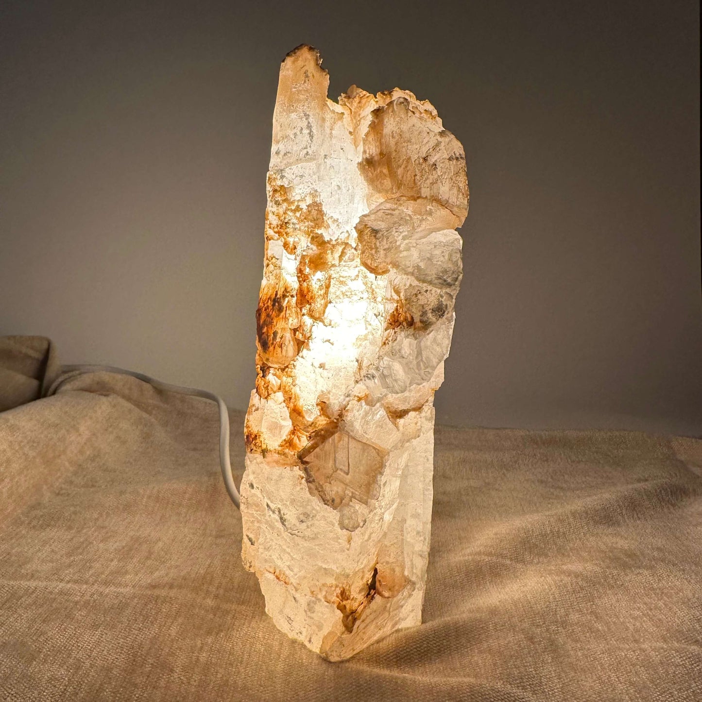 Mexicansk Selenit lampe nr 5 lyser blødt op med sin naturlige stenskønhed på en tekstureret beige overflade.