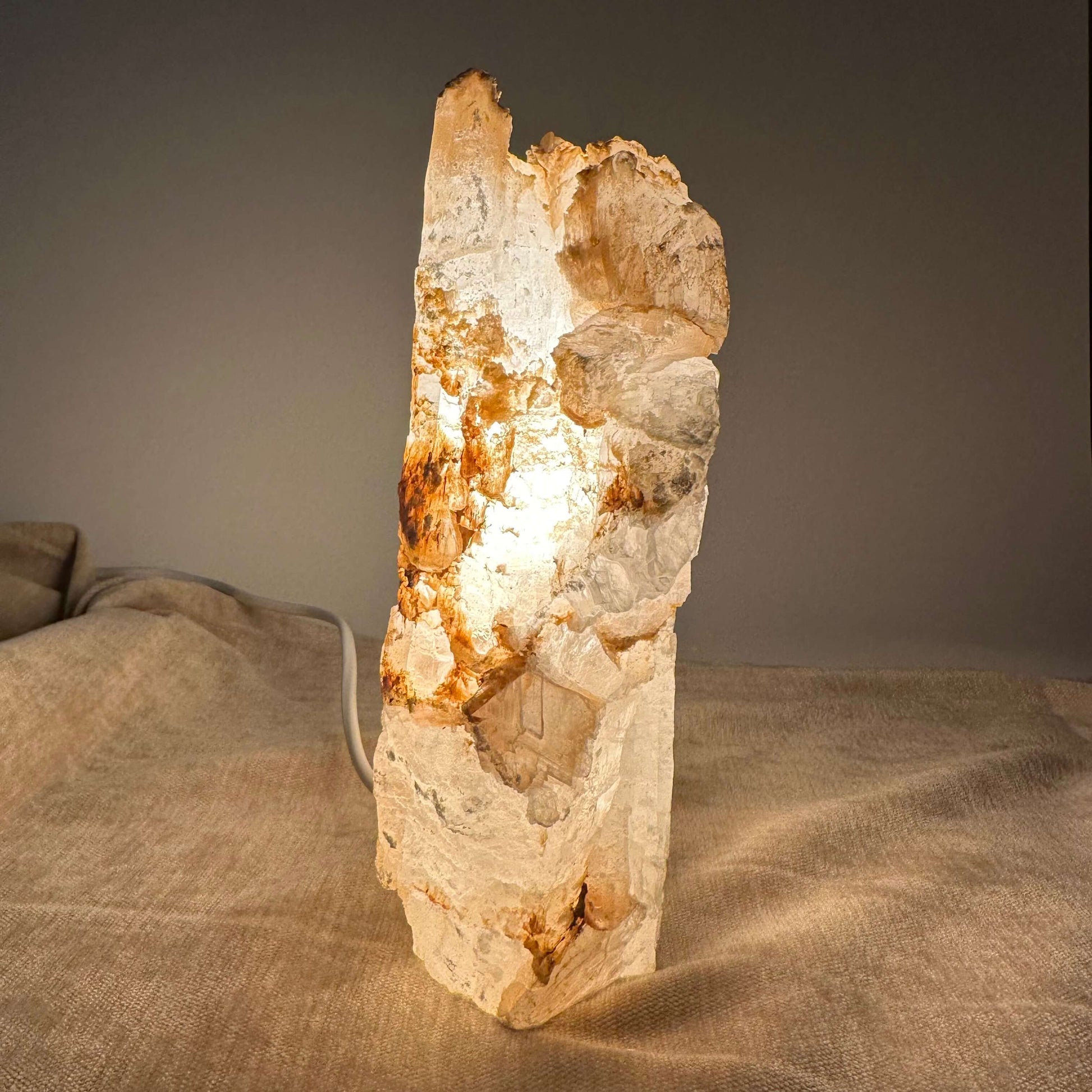 Mexicansk Selenit lampe nr 5 lyser blødt op med sin naturlige stenskønhed på en tekstureret beige overflade.