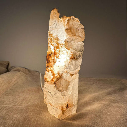 Mexicansk Selenit lampe nr 5 lyser blødt op med sin naturlige stenskønhed på en tekstureret beige overflade.