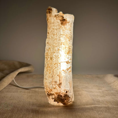Mexicansk Selenit lampe nr 26 lyser op på en stofbelagt overflade i dæmpet belysning.