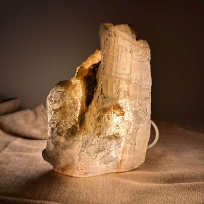 Mexicansk Selenit lampe nr 27 lyser blødt op, stående på en tekstureret overflade i dæmpet belysning.