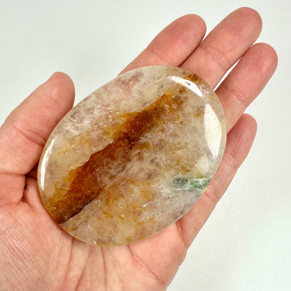 En hånd holder en oval golden healer skive med gule og orange mønstre.