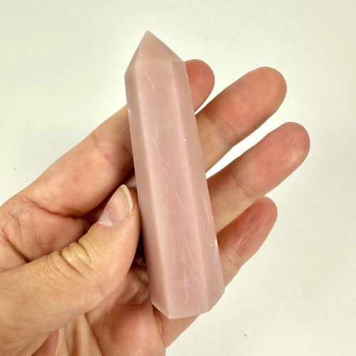 Hånd holder et pink opal tårn mod en hvid baggrund.